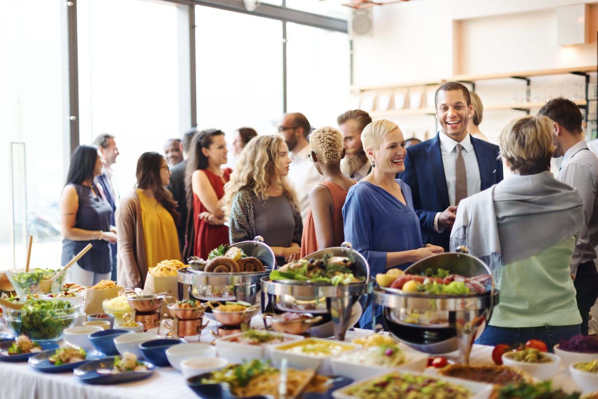 Guests networking around a buffet at a professionally catered corporate event in a modern venue.